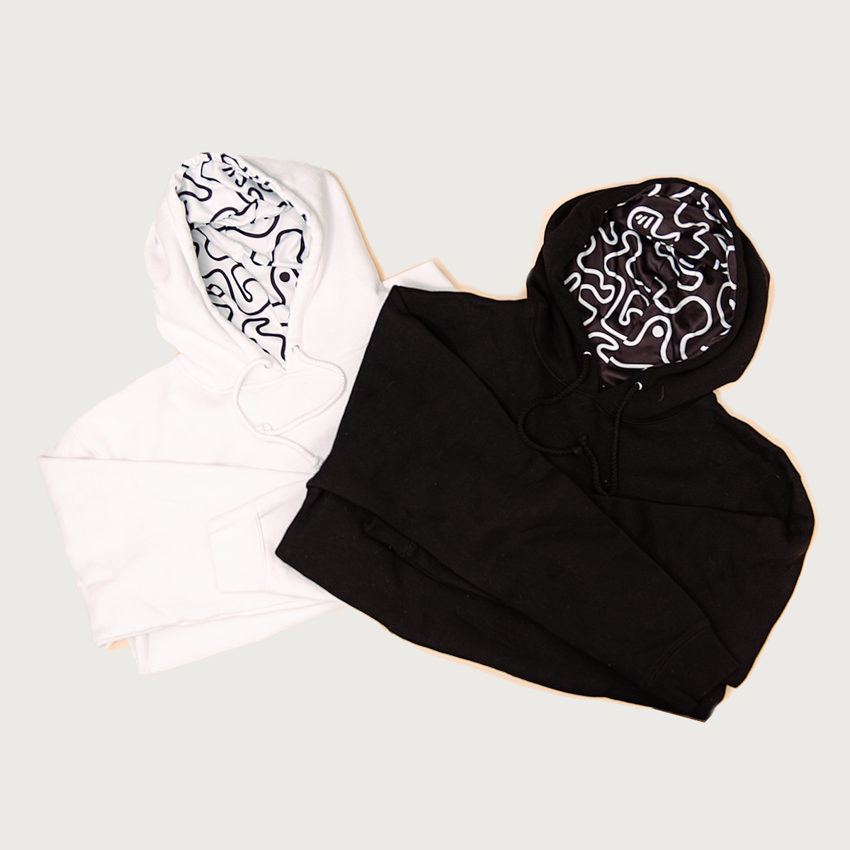 Cozy lined hoodies folded in both black and white with a monochromatic raised MAD TASTY logo and hoodie lined with our signature squiggle line art.